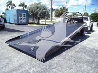 Ram 2024 Ram 5500 SLT rollback chassis with a raised flatbed on a white tow truck in a dealership lot; long black flatbed with tie-down chains and a winch area visible.
