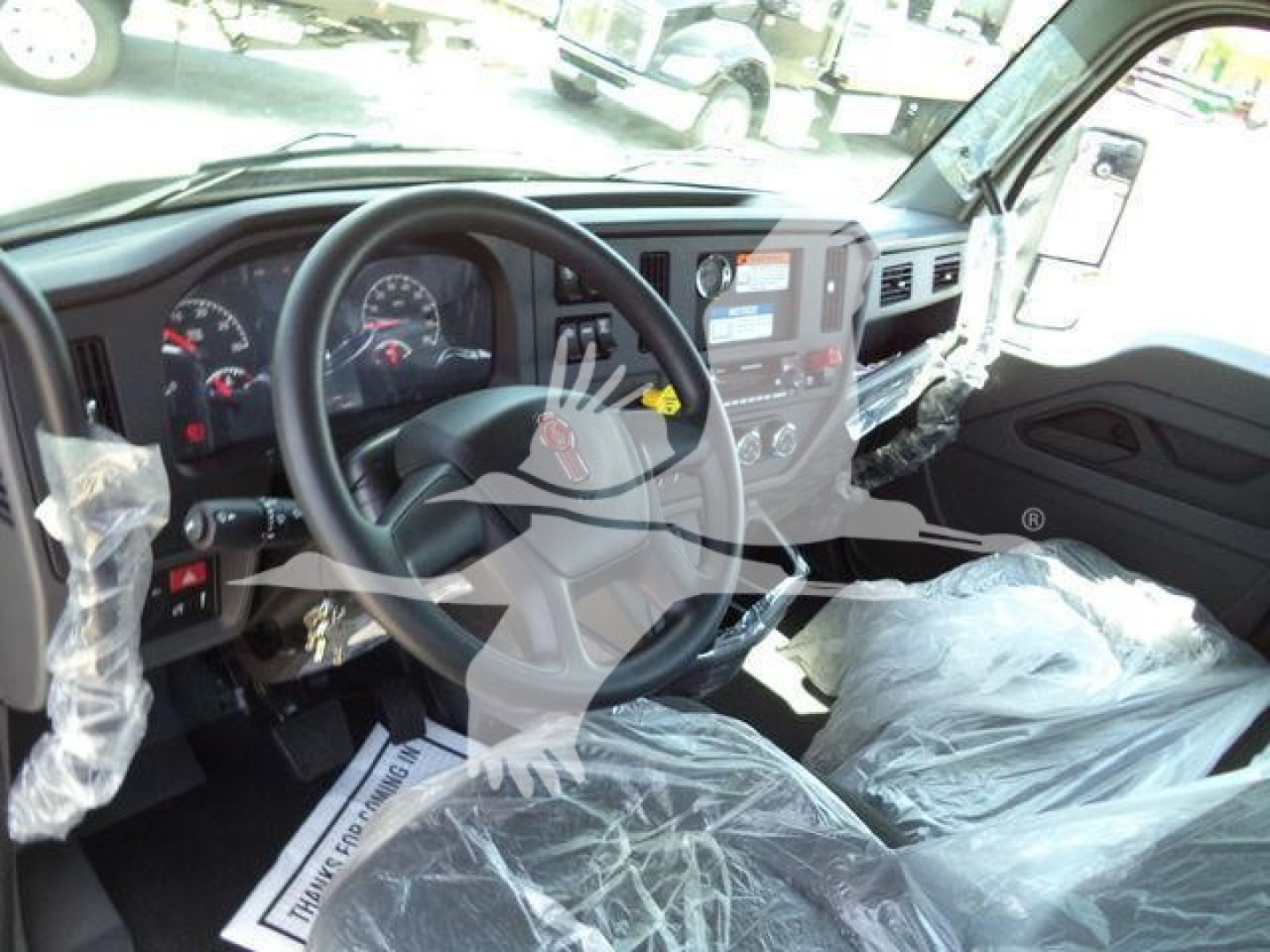 Truck cab interior of a new Kenworth T280 rollback showing steering wheel, dashboard, and plastic-covered seats with stock papers in cabin.