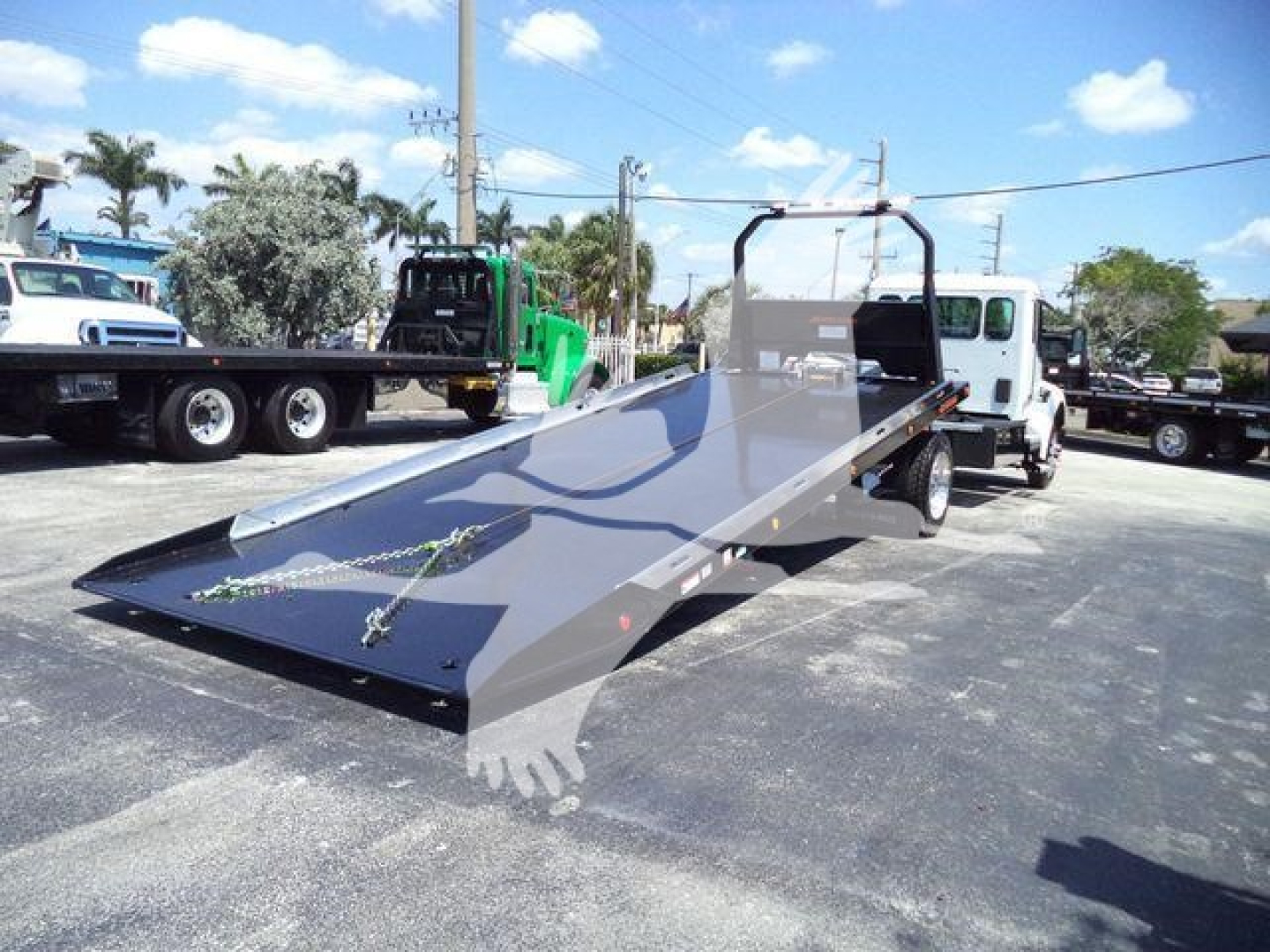 Flatbed tow truck with a long gray steel ramp in a parking lot, Kenworth T280 rollback truck in background, stock number KWT280XLPSHARK.