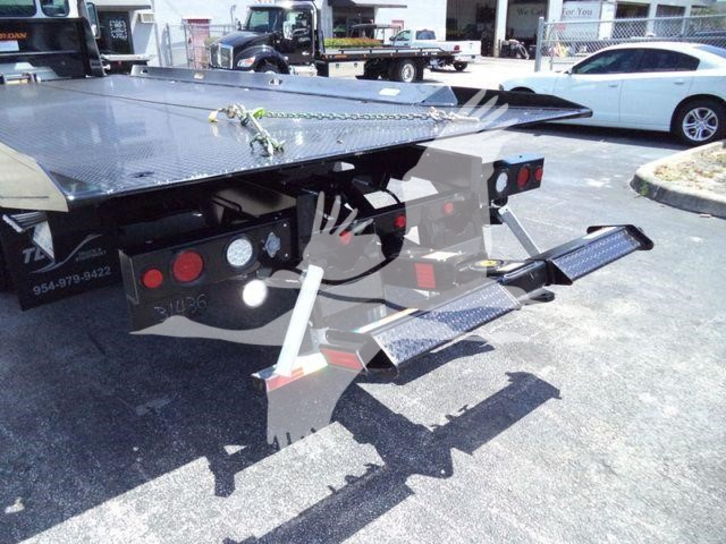 Trailer hitch with dual rear outriggers and safety chains on a flatbed rollback truck bed showing metal steps and platform edges.