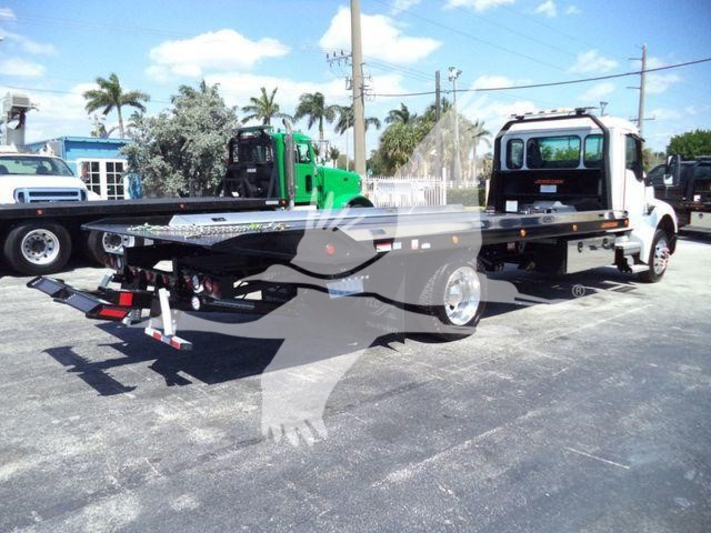 Kenworth T280 rollback truck chassis with flatbed, rear view showing ramps and hydraulic system, daytime outdoor lot.