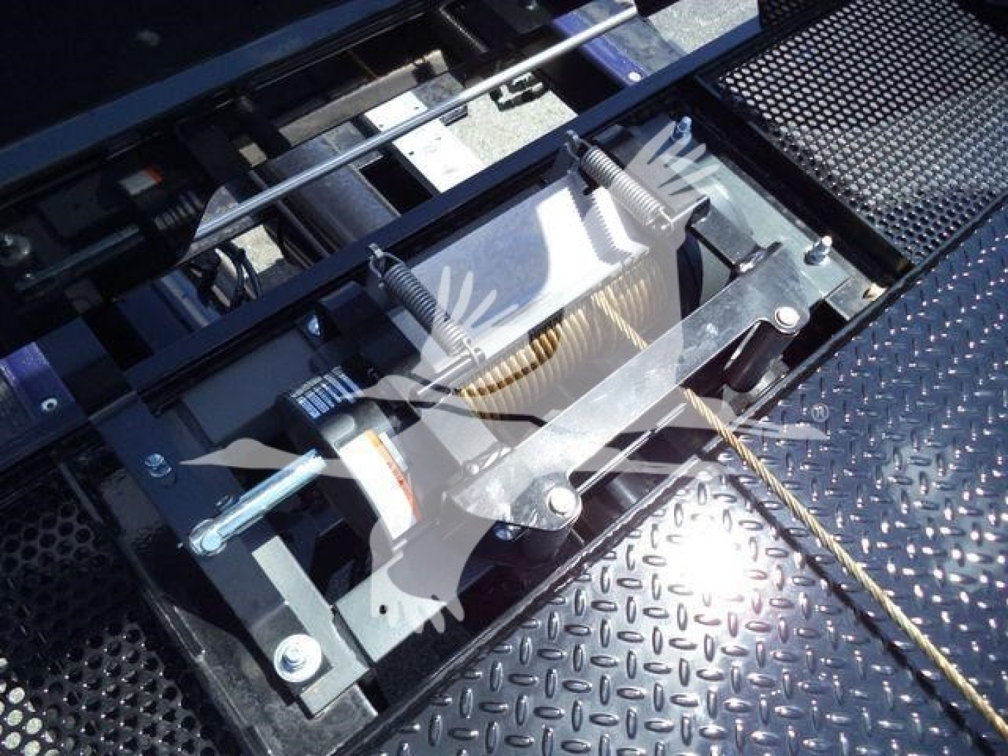Kenworth truck rollback setup showing hydraulic winch mechanism with bolts and metal plates, diamond plate platform, and cables.
