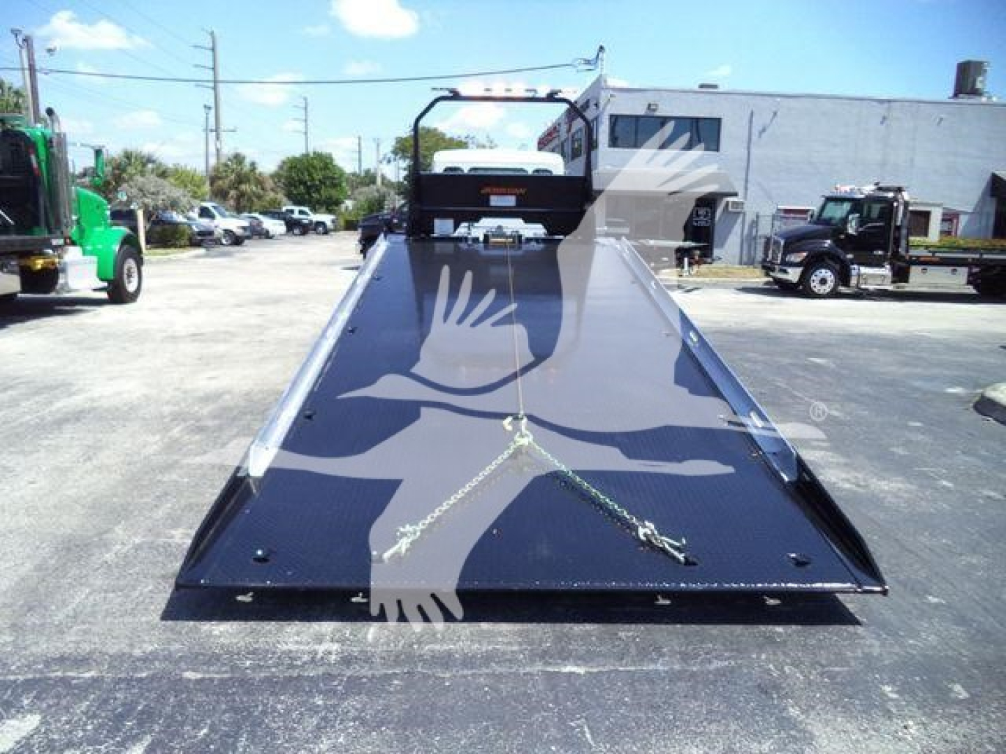 Kenworth T280 rollback truck bed in front view, with hydraulic ramps and winch area, blue-black glossy surface, open lot with other trucks in background.
