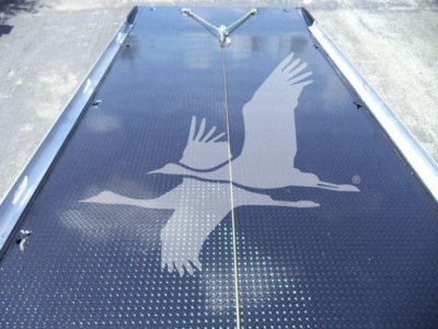 Truck rollback bed with a large white bird decal on the black diamond plate surface, centerline tie-down points visible.
