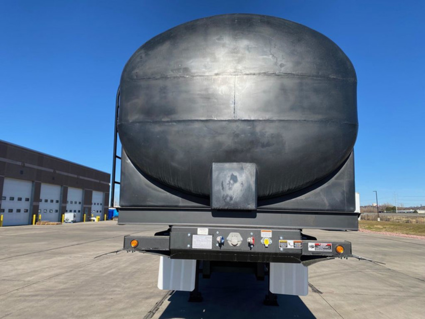 Rear view of a Demco liquid tender trailer tank showing circular black tank and underside controls with warning labels.