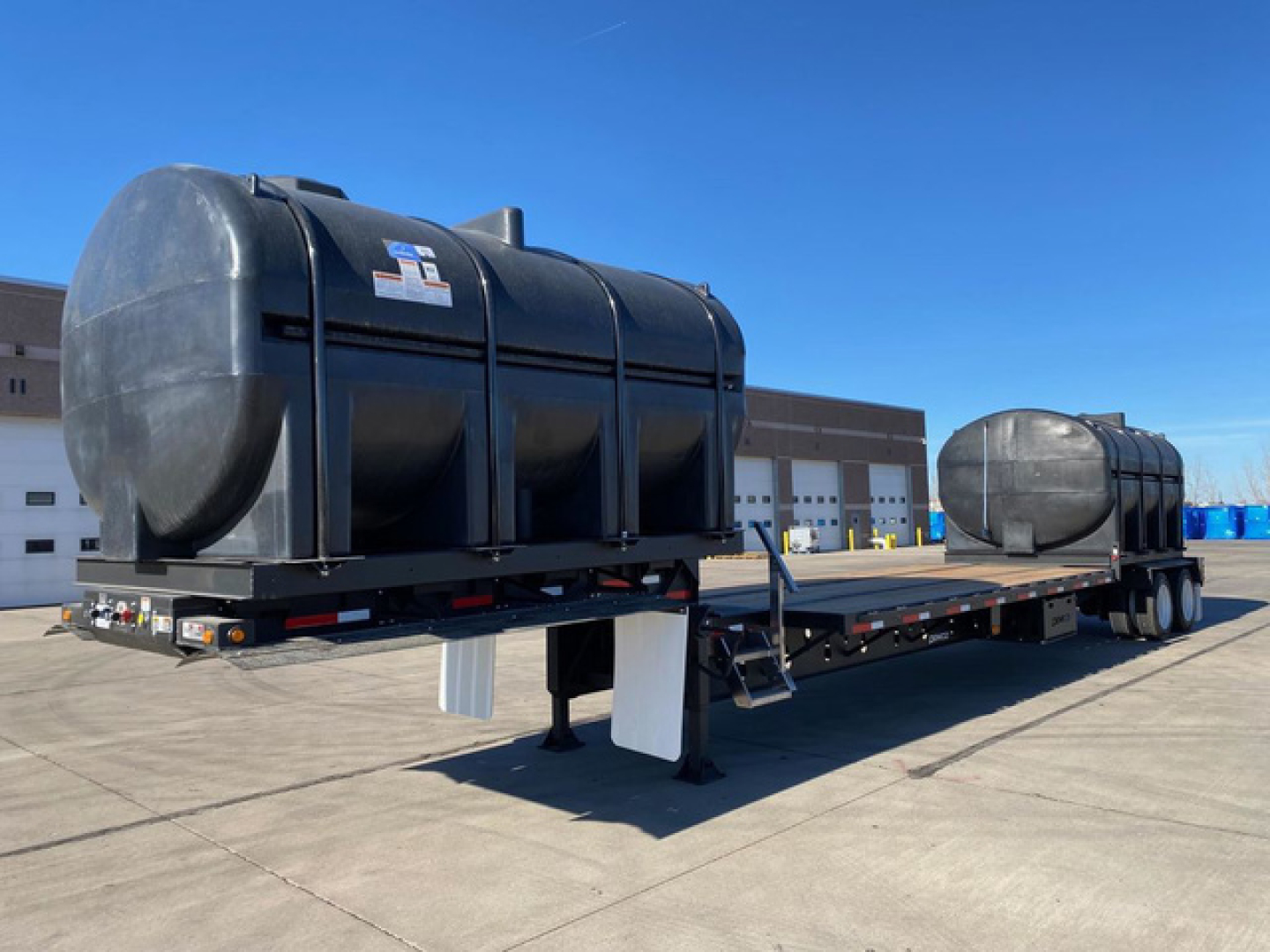 Demco Liquid Tender trailer on flatbed show exterior tank with support legs and trailer hitch in clear daylight.