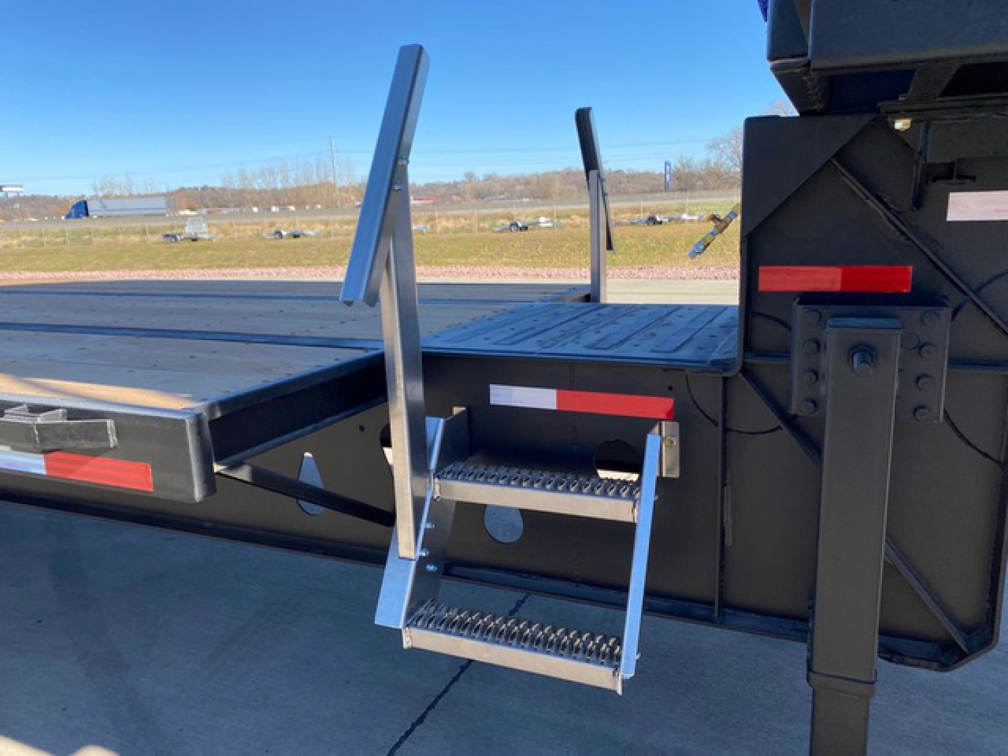 Trailer side view showing metal steps with anti-slip treads and a fold-down ladder attached to a Demco Liquid Tender trailer.