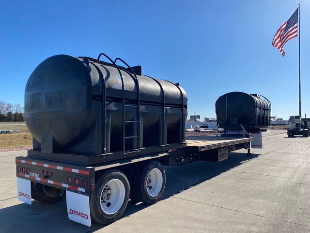 Demco Liquid Tender trailer in new condition on a flatbed, two tanks mounted on a long trailer with wheels, American flag in background, VIN 007207 and stock N87047 visible in listing