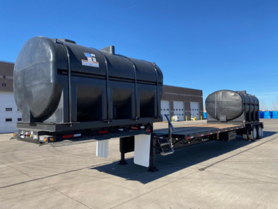 Demco Liquid Tender trailer on flatbed show exterior tank with support legs and trailer hitch in clear daylight.