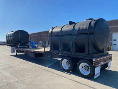 Demco Liquid Tender trailer showing large black cylindrical tank on dual-axle flatbed trailer with safety rails and rear mudflaps.