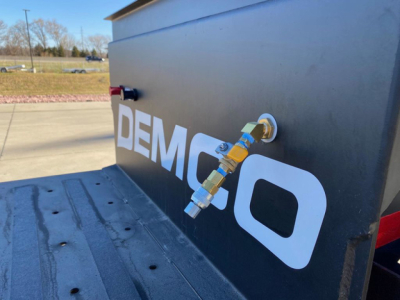 Demco liquid tender trailer exterior with connection fittings and 'DEMCO' logo visible on black side panel.