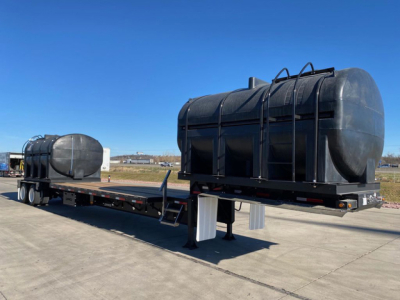 Demco Liquid Tender trailer tanks on a lowboy trailer showing twin cylindrical black tanks with ladders and support frames.