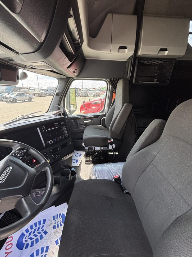Cab interior of a Freightliner Cascadia 126 truck showing driver seat, steering wheel, and dashboard amid white overhead cabinets.