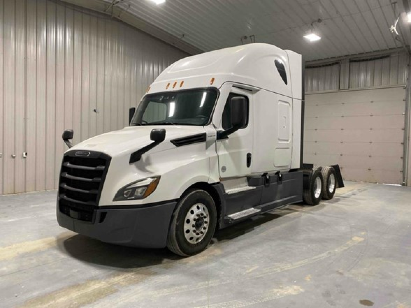 Freightliner Cascadia 126 sleeper cab tractor in a showroom, white exterior with black grille, long nose, 3 axles, no trailer.
