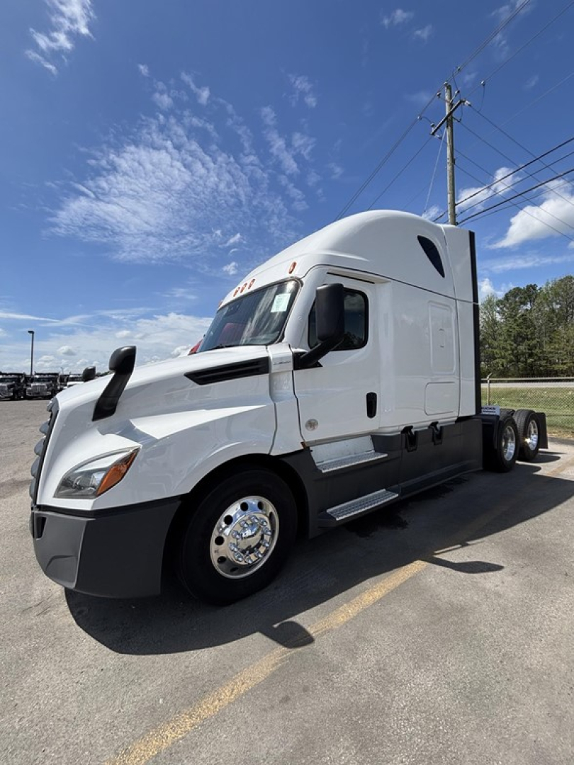 Freightliner Cascadia 126 sleeper cab tractor in a parking lot, side view showing front hood, side steps, aerodynamic mirrors, and dual rear axles.