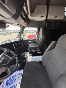Cab interior of a Freightliner Cascadia 126 truck showing driver seat, steering wheel, and dashboard amid white overhead cabinets.