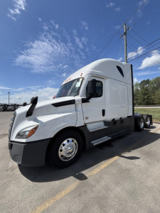 Freightliner Cascadia 126 sleeper cab tractor in a parking lot, side view showing front hood, side steps, aerodynamic mirrors, and dual rear axles.