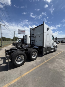 Truck chassis and cab of a 2023 Freightliner Cascadia 126 in a parking lot showing the rear triple axles and sleeper cab.