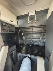Truck sleeper cab interior with bunk area and storage netting; visible latch and panel in upper wall, no legible labels or text.