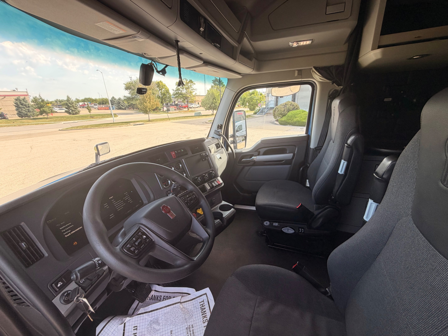 Kenworth truck cabin interior showing driver's seat, steering wheel, and dashboard with control panels and center console.