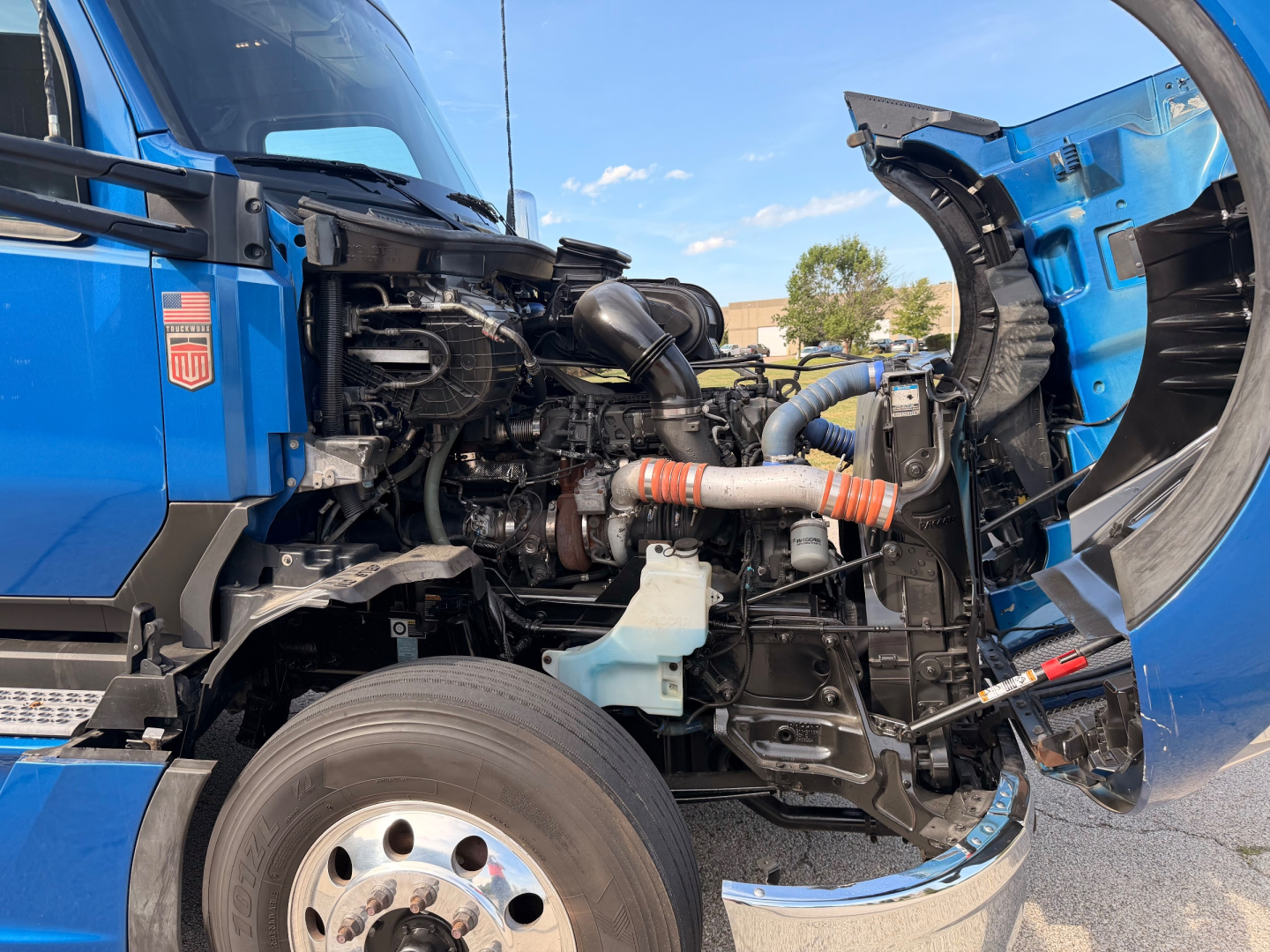 Truck engine bay of a 2022 Kenworth T680 with hood open, showing turbocharger, hoses, coolant reservoir, and diesel engine components.