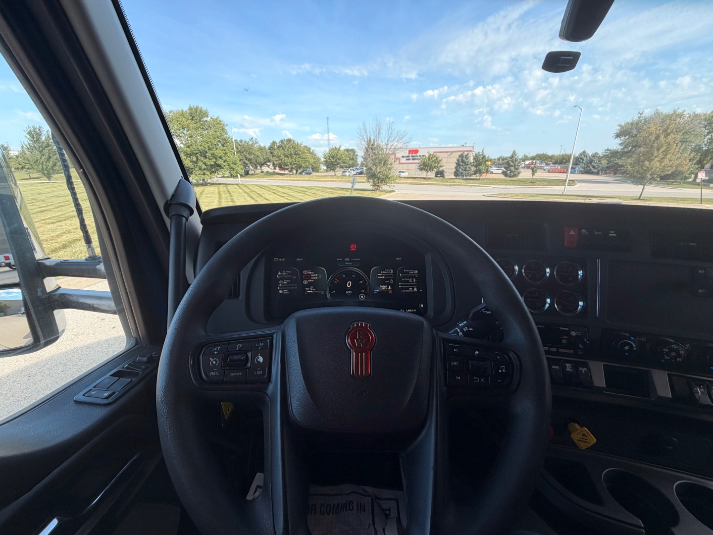 Kenworth T680 interior driver's seat and dashboard with steering wheel, instrument cluster, and center controls visible; window shows outdoor scene.