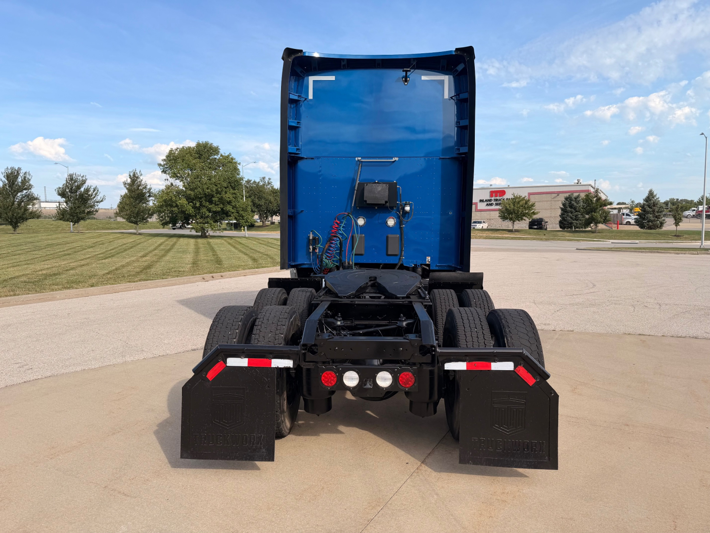 Kenworth truck rear view showing chassis and blue sleeper cab, dual rear axles, mud flaps, and side reflectors.