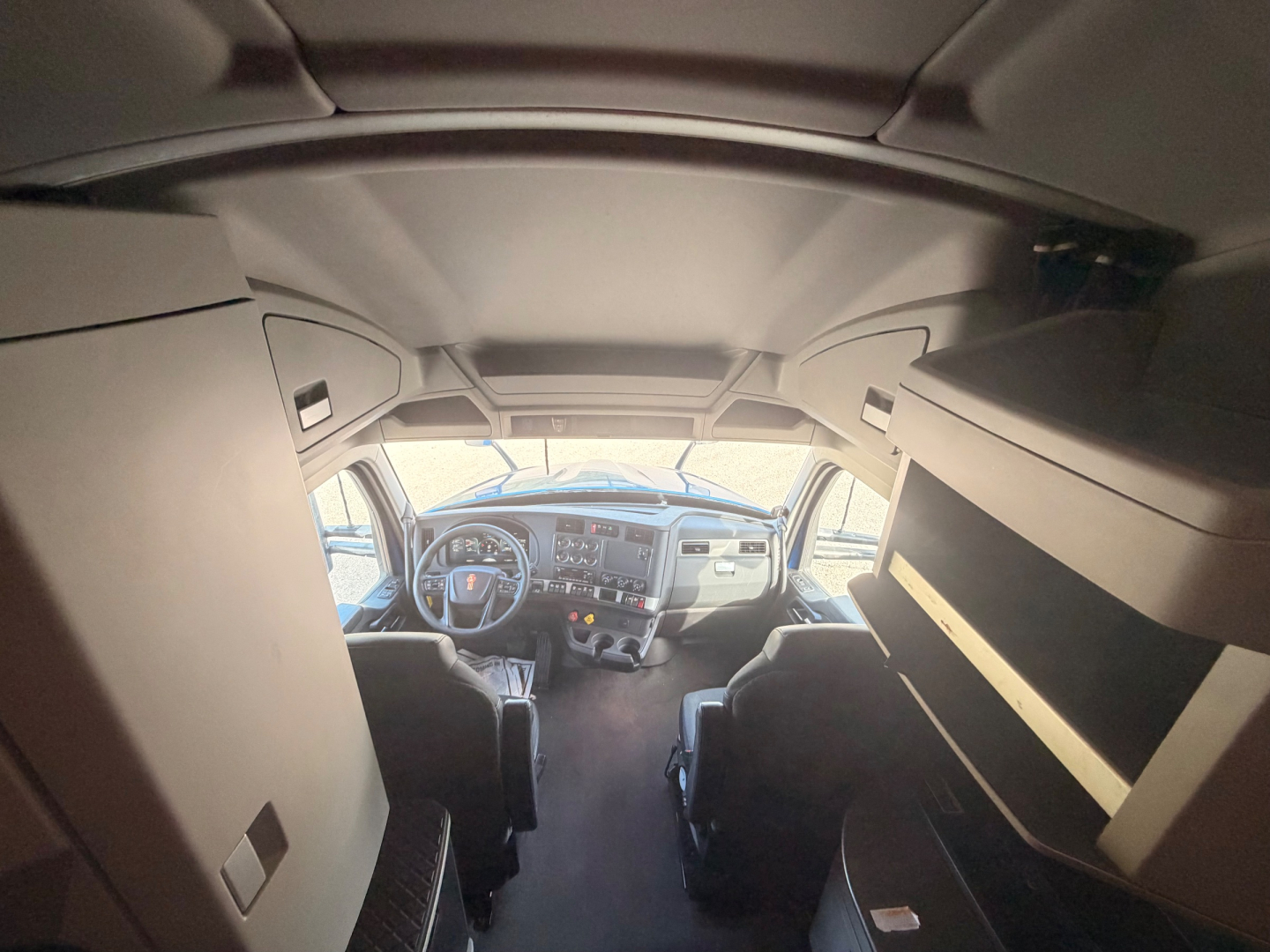 Kenworth T680 cab interior view showing dash and driver seat area, overhead storage and sleeper cab side shelves.