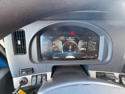 Truck dash and steering wheel of a Kenworth T680 showing a digital instrument cluster. Nozzle controls and dashboard elements visible.