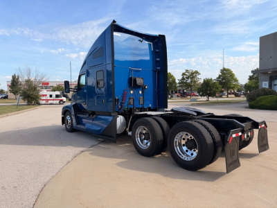 Kenworth T680 tractor cab in blue, rear view showing dual rear axles and fifth wheel, side windows, and aerodynamic sleeper with chrome wheels.