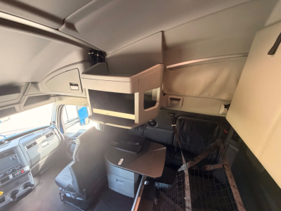 Kenworth T680 interior sleeper cab with overhead bunk storage shelf and desk area, view toward driver seat and dashboard.
