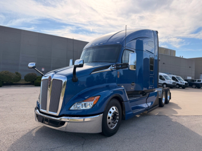 Blue Kenworth T680 tractor in a parking lot with chrome grille, headlights, and large side mirrors; no visible text on the vehicle.