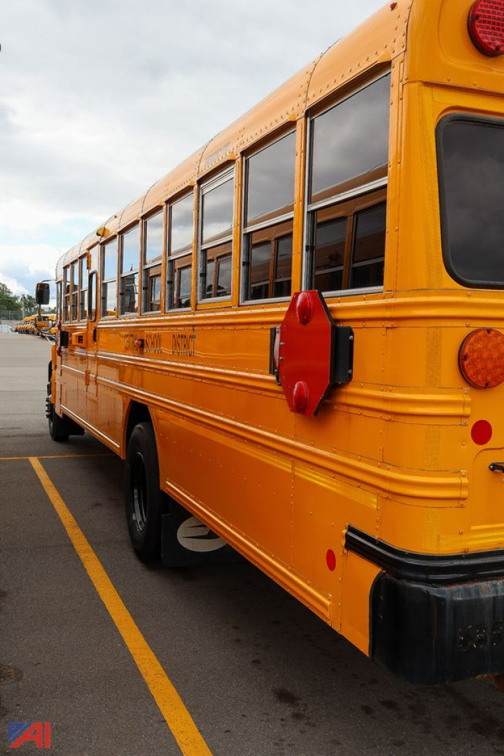 School bus side view showing yellow body, black bumper, red reflectors, and multiple windows along the passenger side.