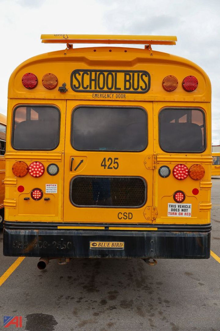 School bus rear view showing yellow body, 'SCHOOL BUS' sign, rear lights, 425 fleet number, CSD emblem, and emergency door; Blue Bird badge on bumper.
