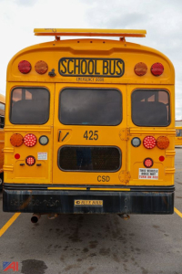 School bus rear view showing yellow body, 'SCHOOL BUS' sign, rear lights, 425 fleet number, CSD emblem, and emergency door; Blue Bird badge on bumper.