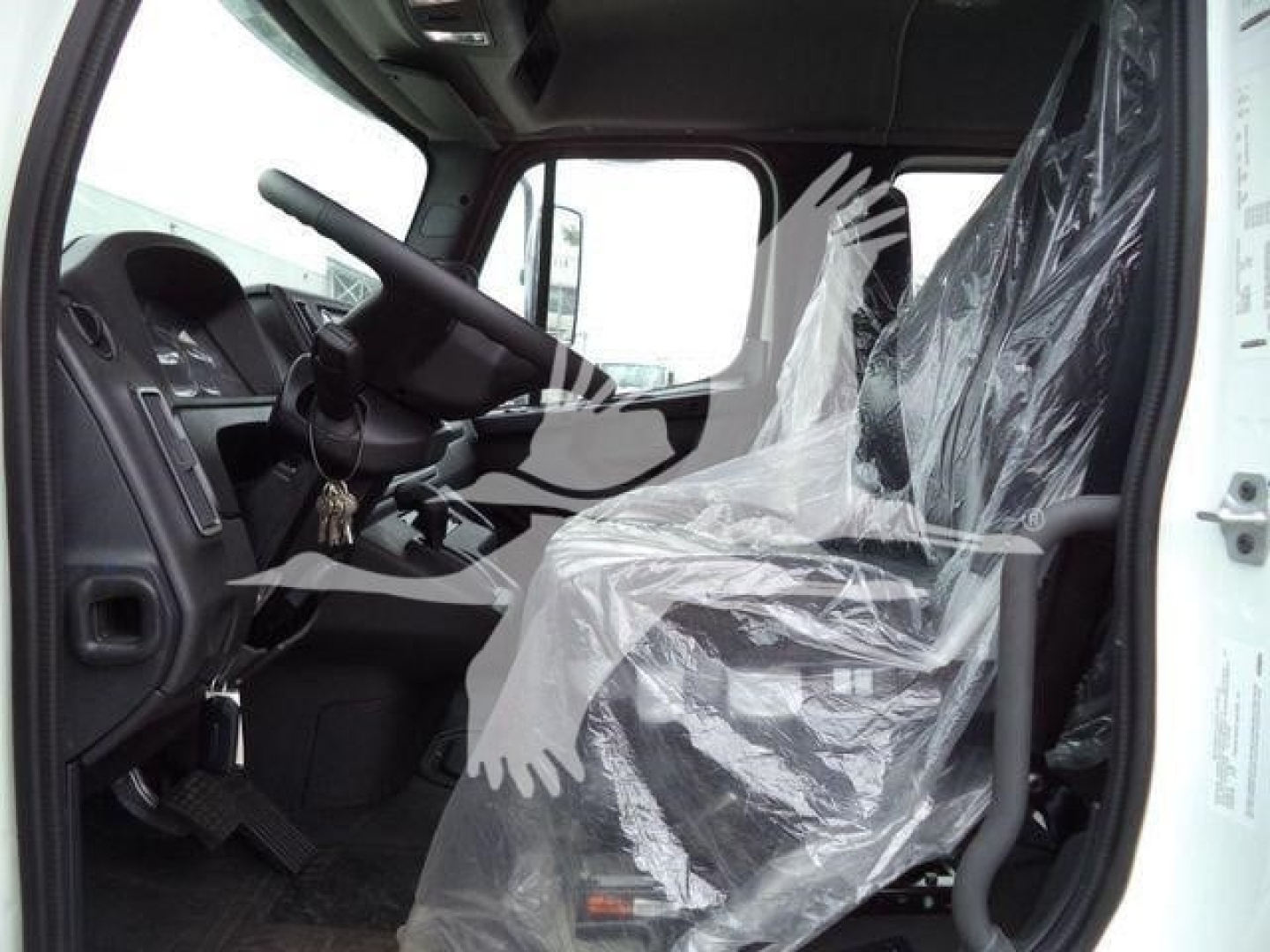 Truck interior cab view of a new Freightliner M2 106 with plastic-wrapped driver seat and steering wheel, dashboard visible.