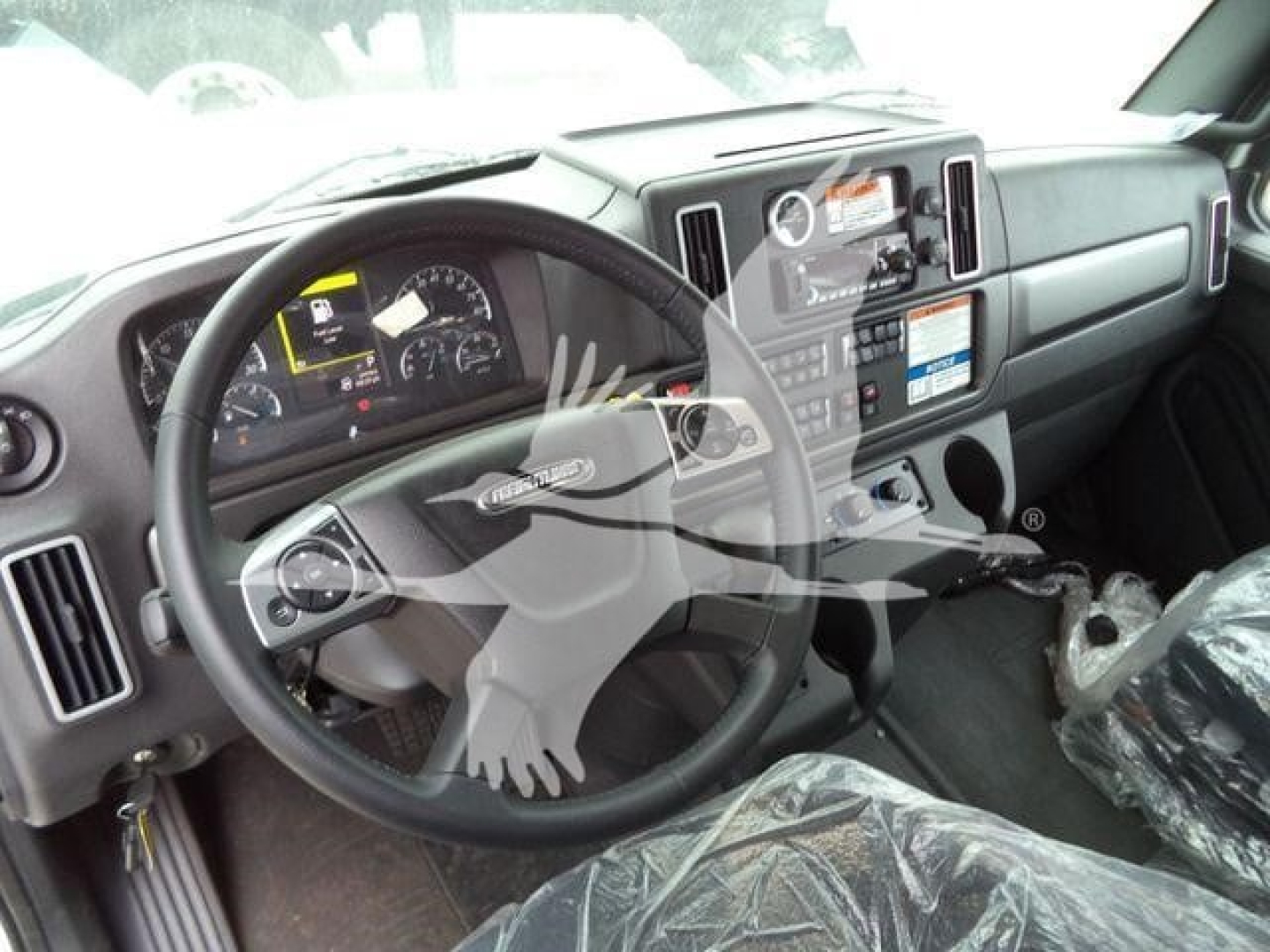 Dashboard and steering wheel of a new Freightliner M2 106 truck interior showing steering wheel, gauges, center console, and protective plastic on the seat.