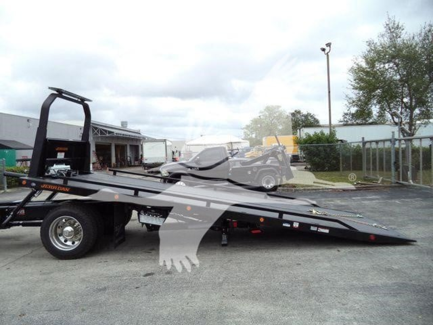 Freightliner M2 106 rollback tow truck flatbed with hydraulic deck and rear-loading ramp; stock yard with overcast sky.