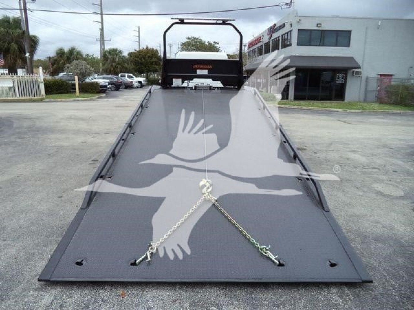 Flatbed of a Freightliner M2 106 rollback truck with a metal ramp and safety chains seen from the front, background shows a dealership building.