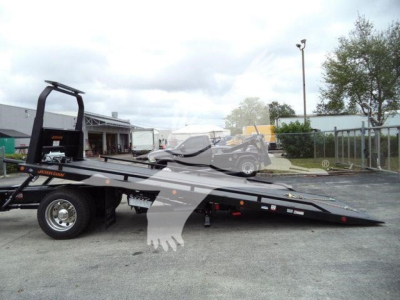 Freightliner M2 106 rollback tow truck flatbed with hydraulic deck and rear-loading ramp; stock yard with overcast sky.