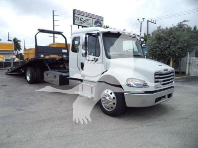 Truck cab and rollback flatbed with crane, white Freightliner M2 106 front view, side door, chrome wheels, dealership lot in background.