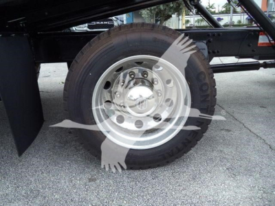 Truck wheel and hub revealing steel wheel with multiple lug nuts and black tire; surrounding frame of Freightliner M2 106 rollback chassis.