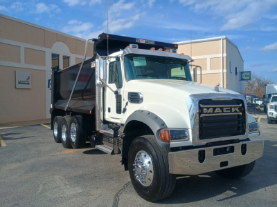 Mack GR84F dump truck in service-ready condition, white cab, dual rear axles, large chrome grille, dump bed visible, dealership lot in background.