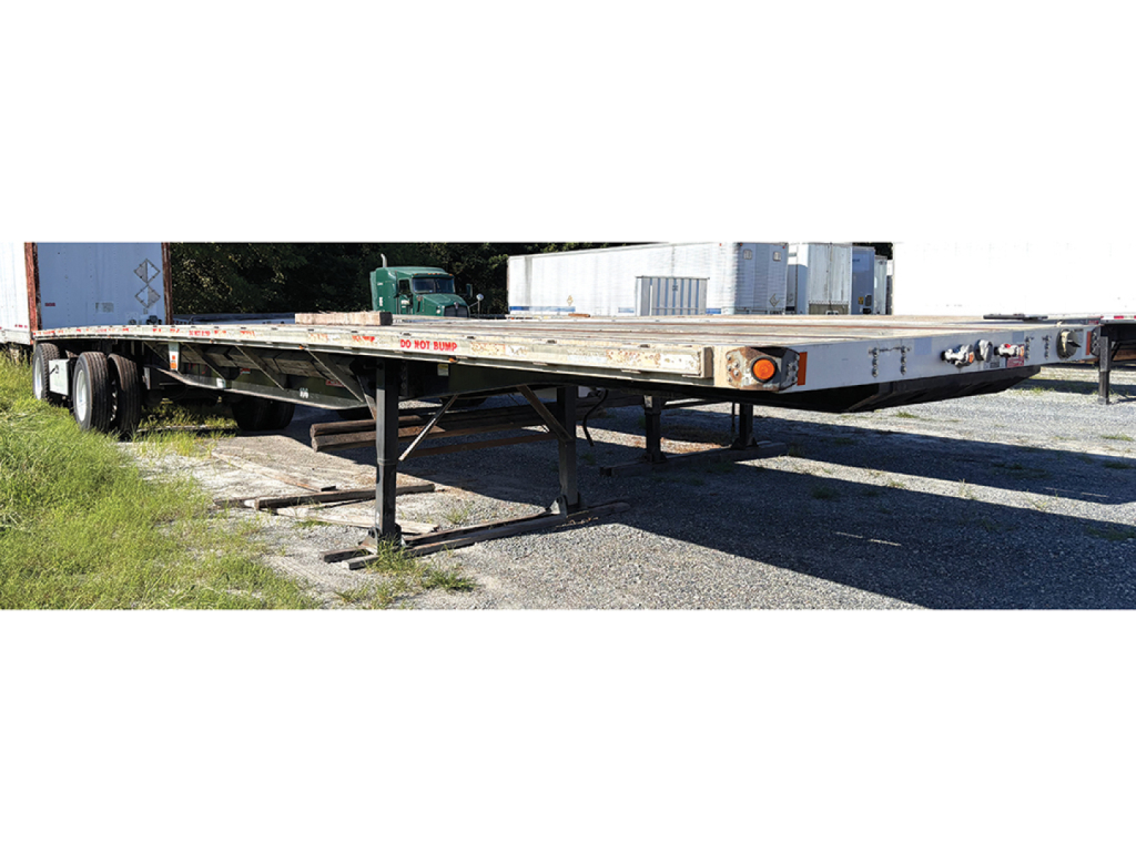 Flatbed trailer in serviceable condition with metal frame and support legs, viewed from side showing deck and undercarriage.