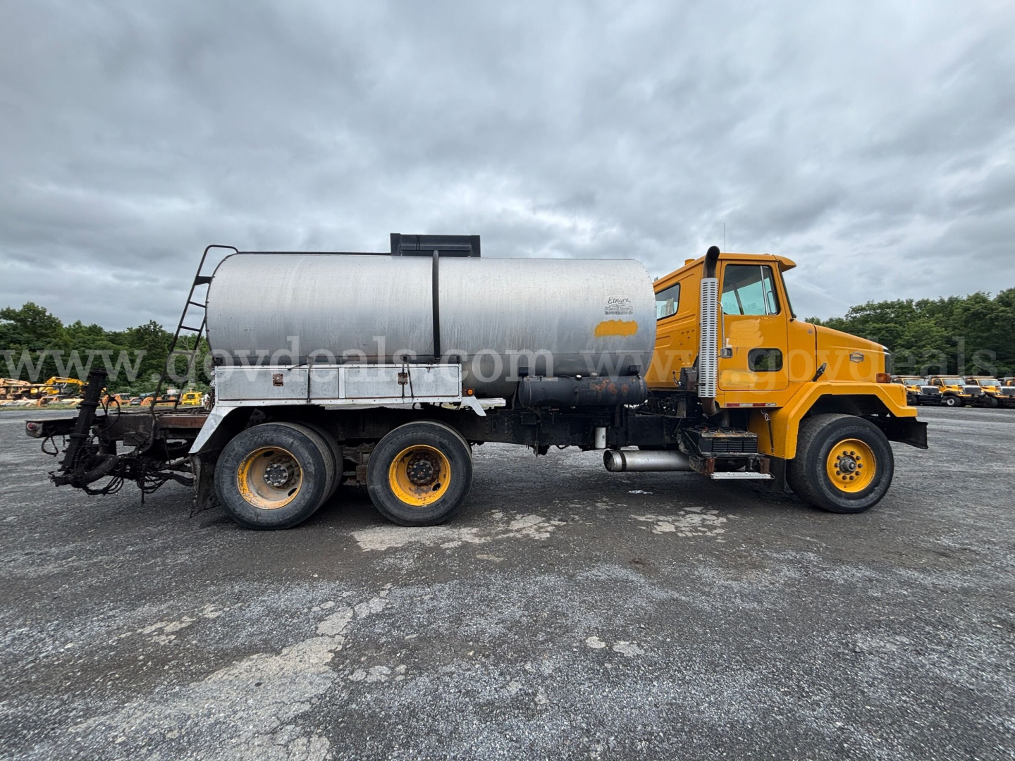 GMC ACL distributor truck side view with yellow cab and cylindrical silver tank in a used equipment lot.