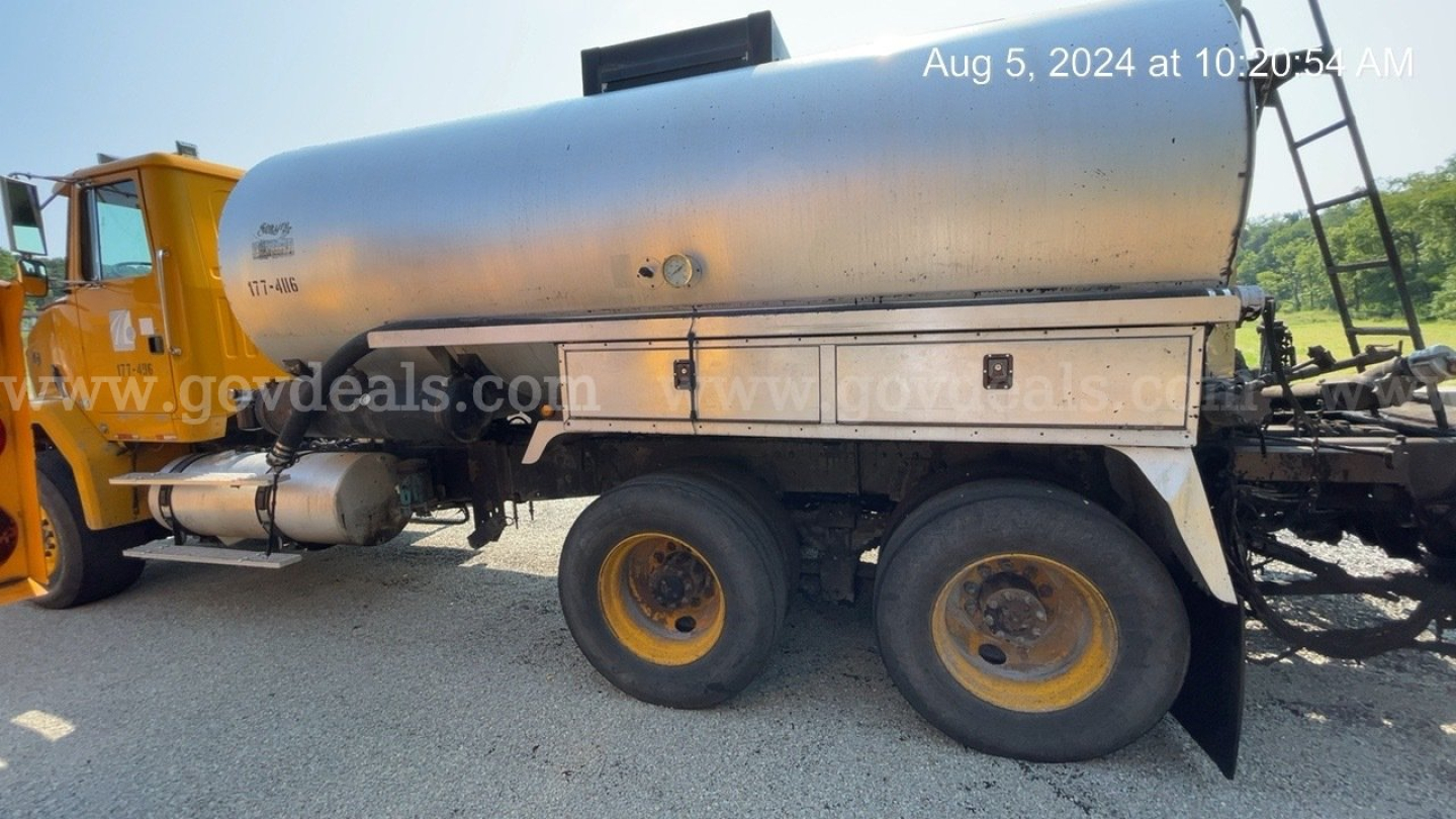 GMC ACL distributor truck with a cylindrical stainless tank, dual rear wheels, and a yellow cab visible on the left; side toolbox and piping along the tank; date stamp in top right.