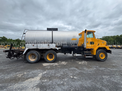 GMC ACL distributor truck side view with yellow cab and cylindrical silver tank in a used equipment lot.
