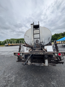 Front view of a white GMC ACL distributor truck trailer with a large circular tank and ladder, showing rear equipment and taillights.
