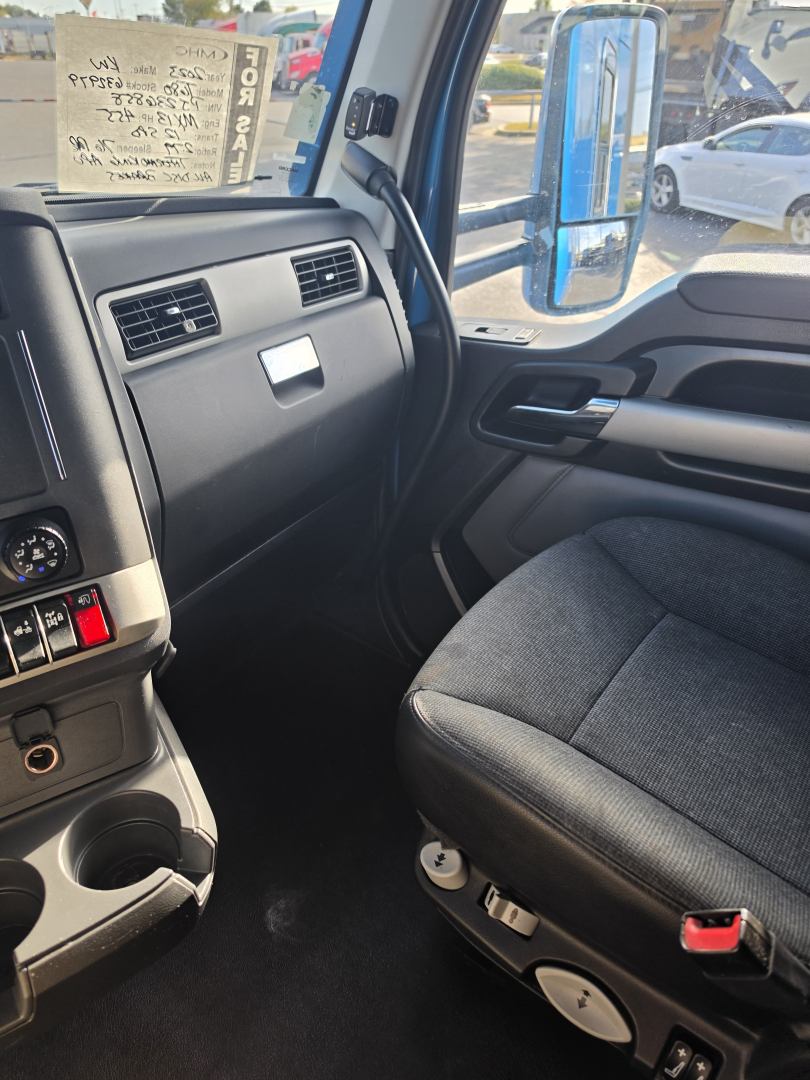 Dashboard and passenger seat area of a Kenworth T680 cabin. Visible text: VIN tag in windshield area, stock/ID card with handwritten notes. Side mirror reflection shows other vehicles.