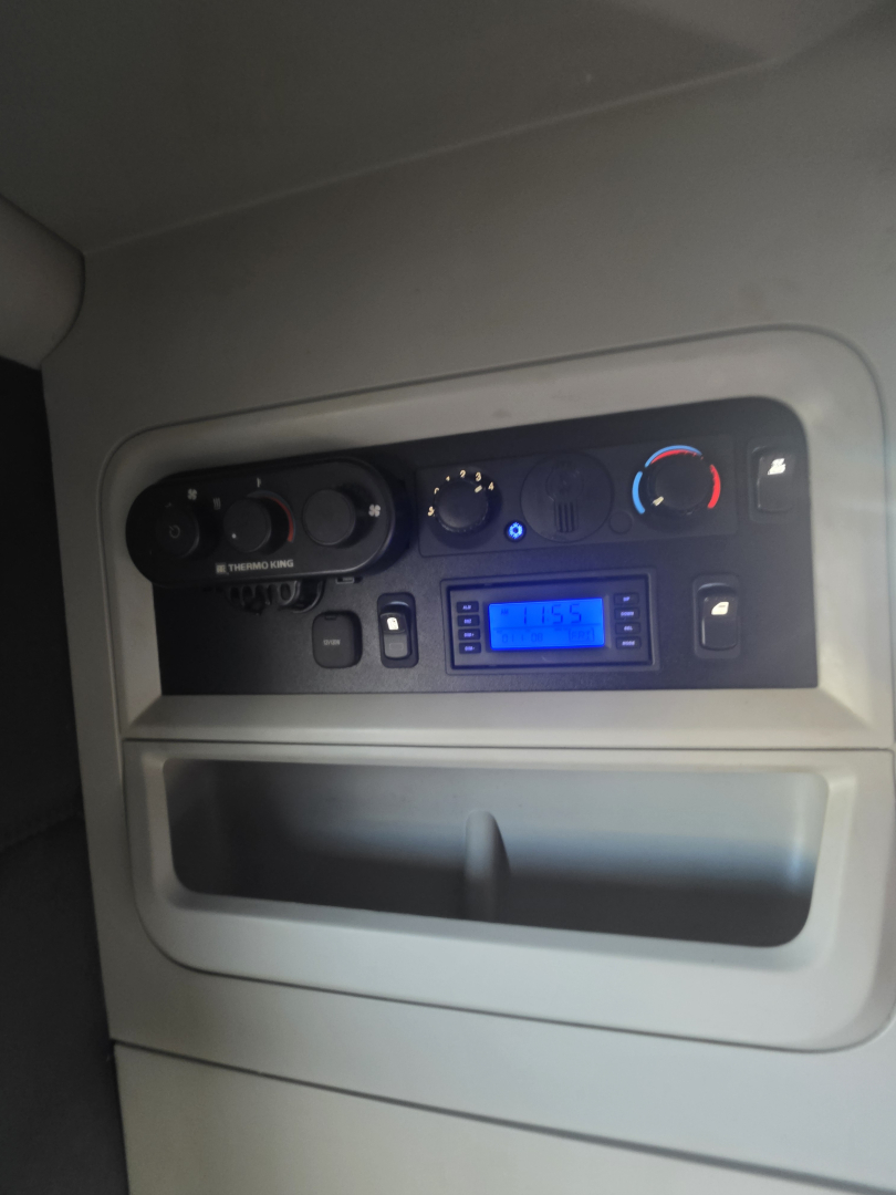 Dashboard panel of a Kenworth truck showing controls, gauges, and a digital display in a sleeper cab with light blue backlit screen.